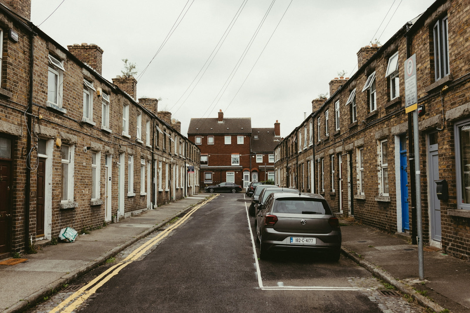 Narrow street lined with traditional terraced houses and parked cars.