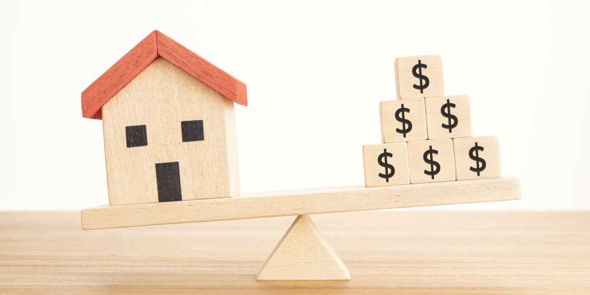 House or Property investment concept. House model and wooden blocks with dollar sign balancing on a seesaw