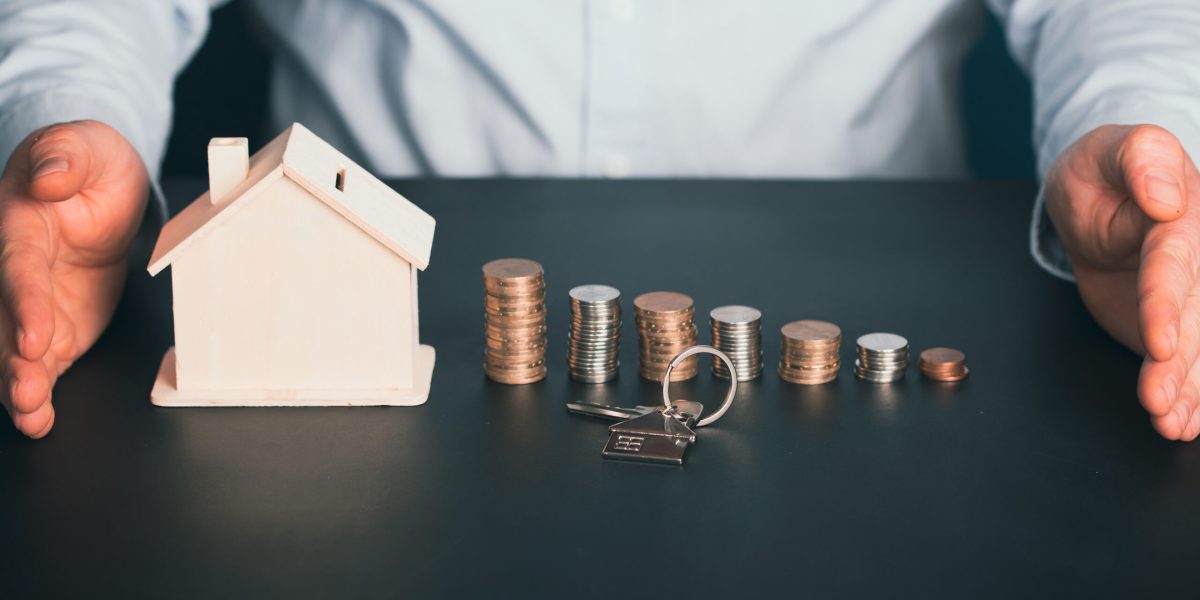 Businessman with house model and piles of coins.Realtor, mortgage, saving money, home loan concept.